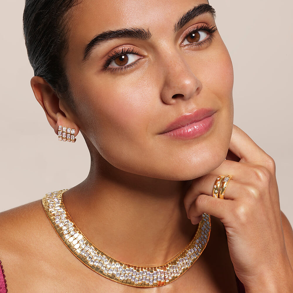 Close-up portrait of a model wearing diamond jewelry, including a necklace, earrings, and rings on a neutral background.