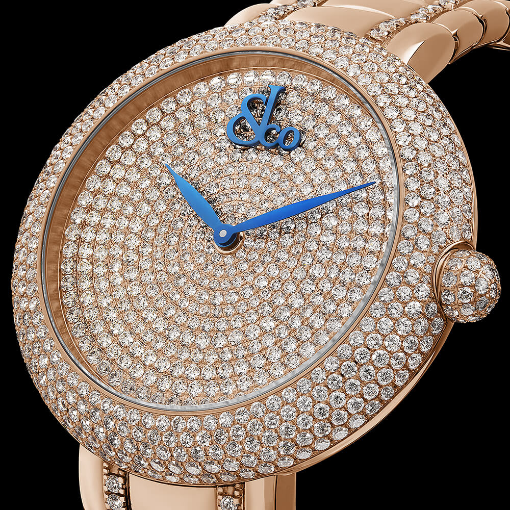 Close-up of a rose-gold watch with a pavé diamond dial and bezel, blue hands, and diamond-set crown.