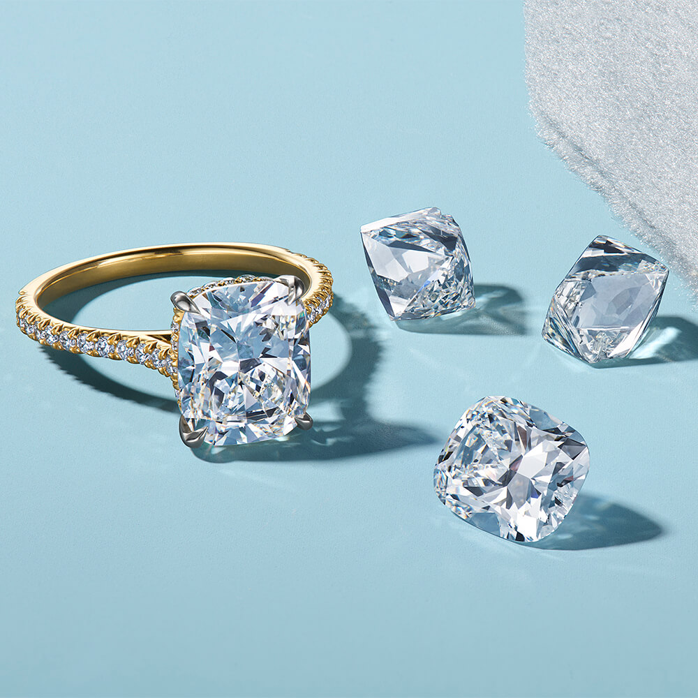 Cushion-cut diamond ring with loose diamonds on a light blue surface, with crisp reflections and shadows.