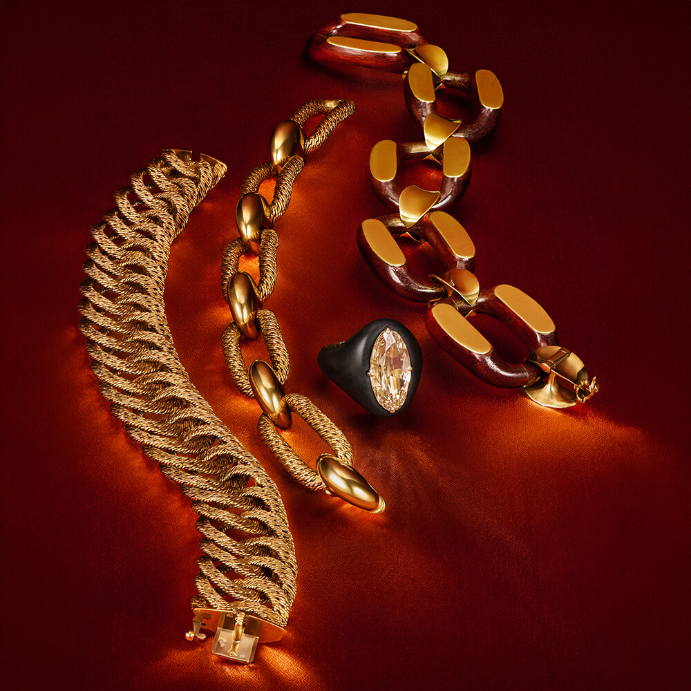 Styled still life of gold jewelry chains and a ring on a rich red background with dramatic lighting.