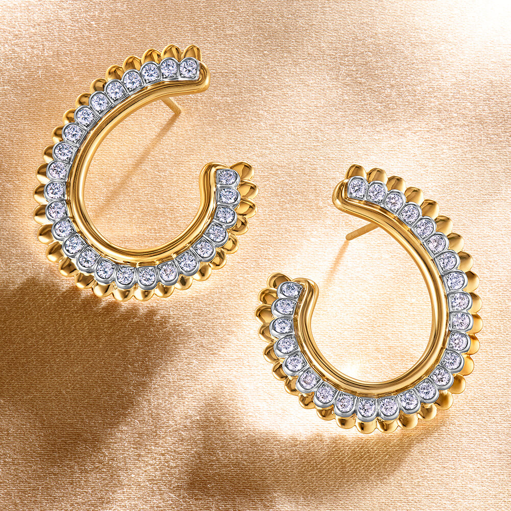 Pair of gold hoop earrings with pavé-set diamonds on a textured gold background.