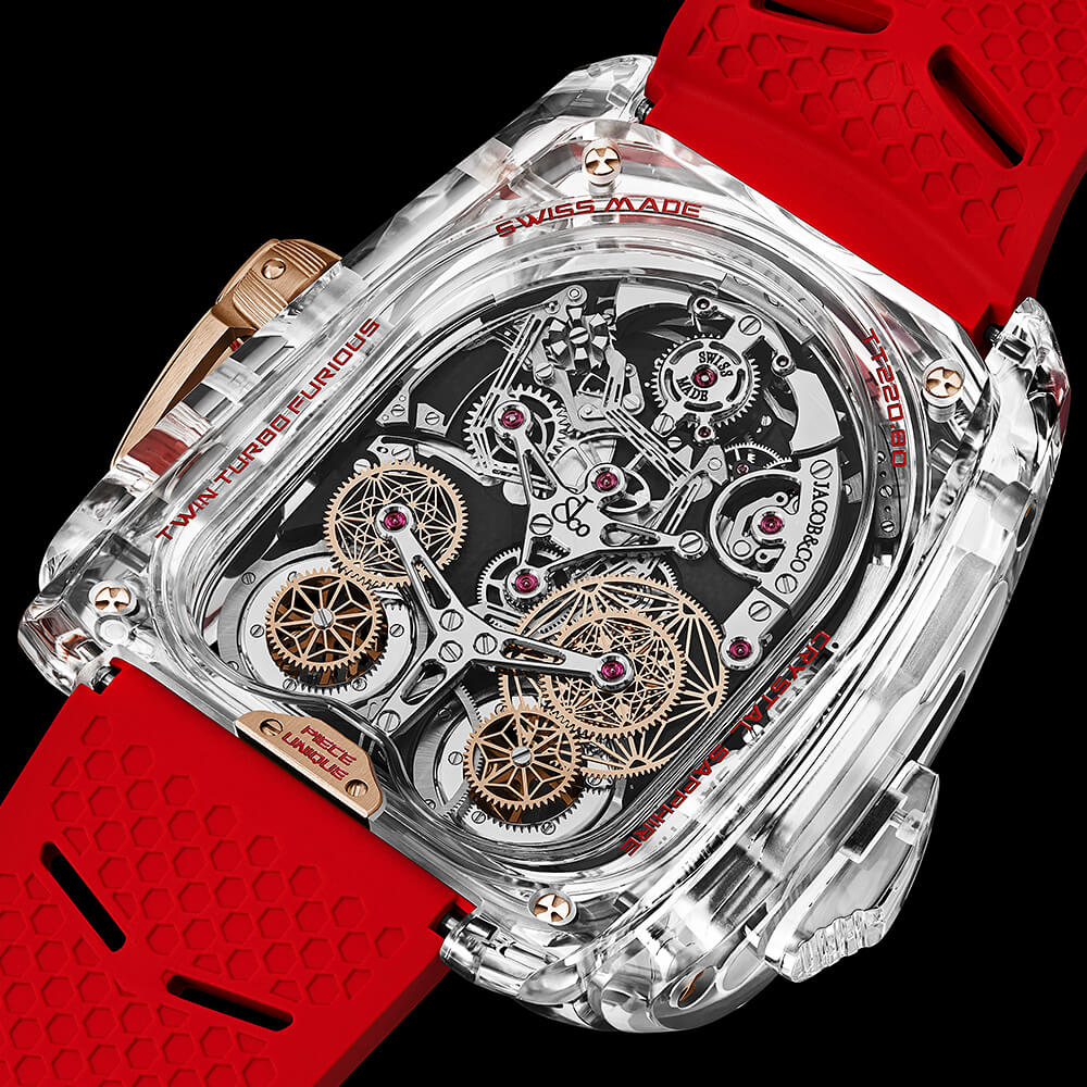 Front view of a high-end watch with a clear crystal case, blue accents, and exposed mechanical movement.